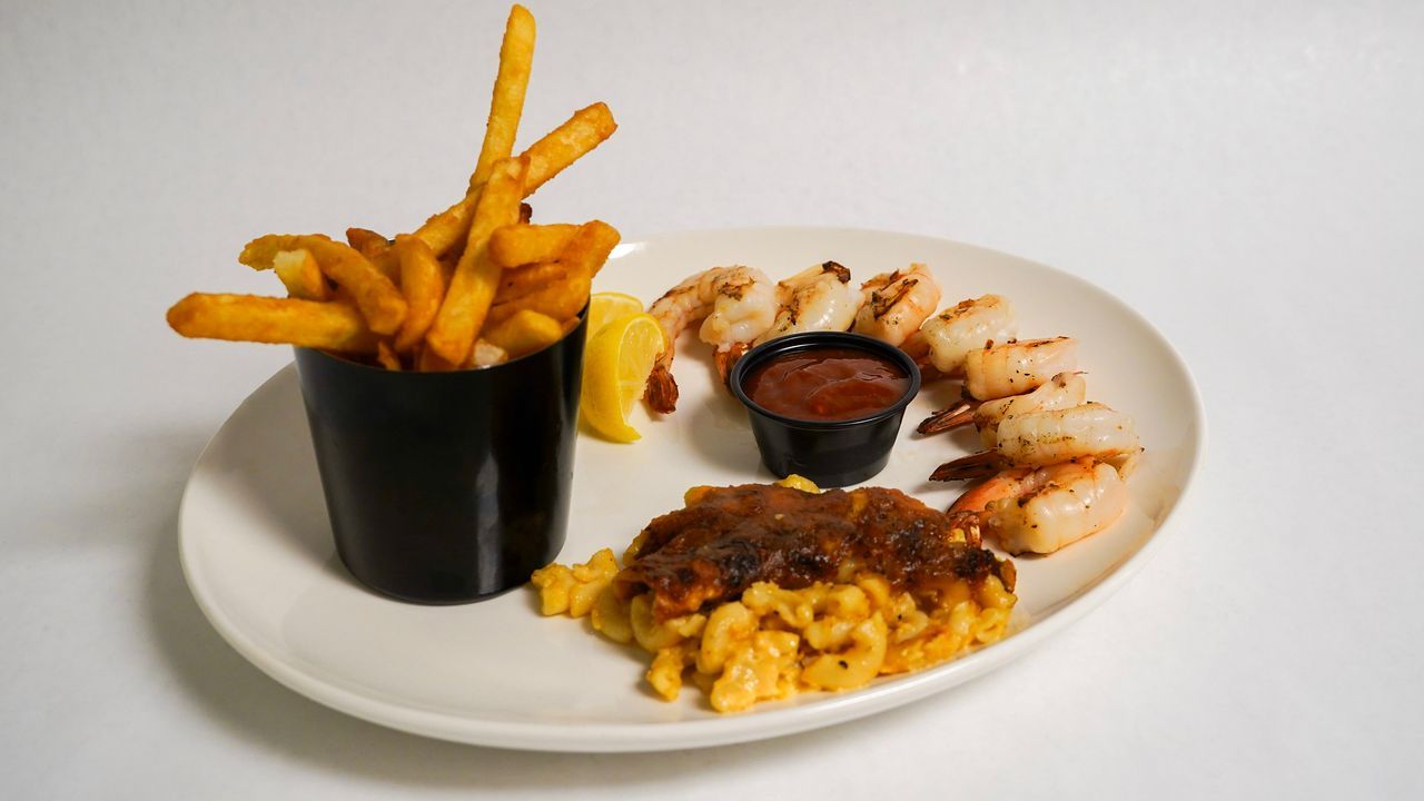 Plate with grilled shrimp, mac and cheese, fries in a cup, and dipping sauce.