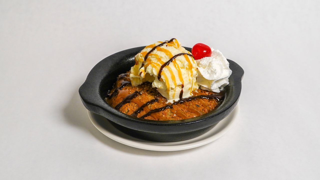 Warm chocolate chip cookie dessert with ice cream, caramel, whipped cream, and cherry.