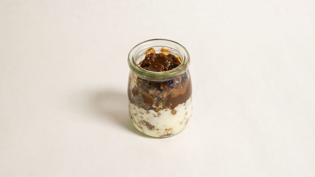 Dessert parfait in a glass jar, layered with cream, chocolate, and toppings.