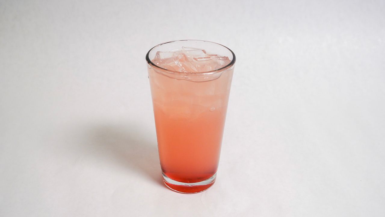 Tall glass filled with a pink-colored beverage and ice, set against a white background.
