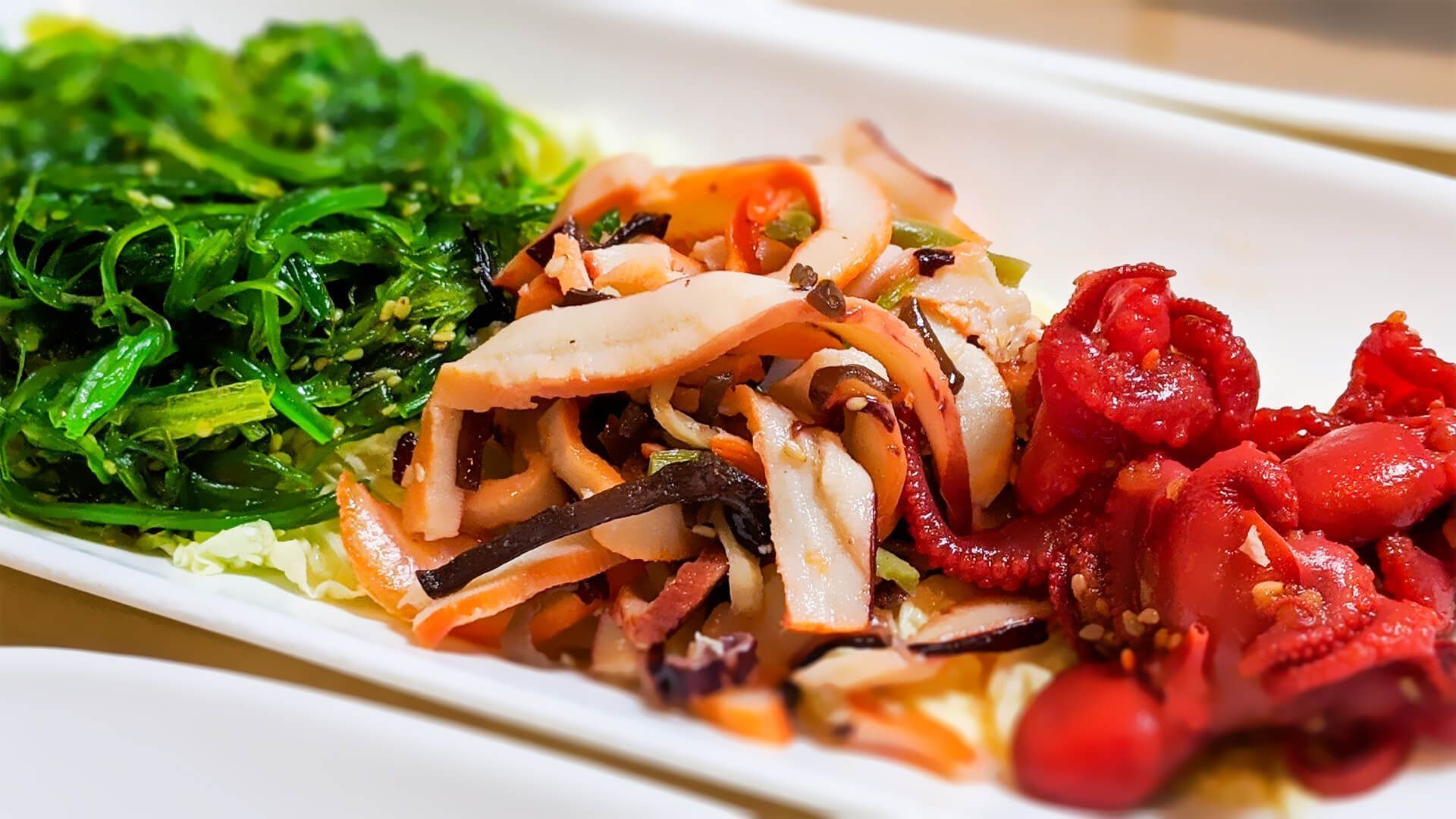 a white plate topped with seaweed, squid, and tomatoes