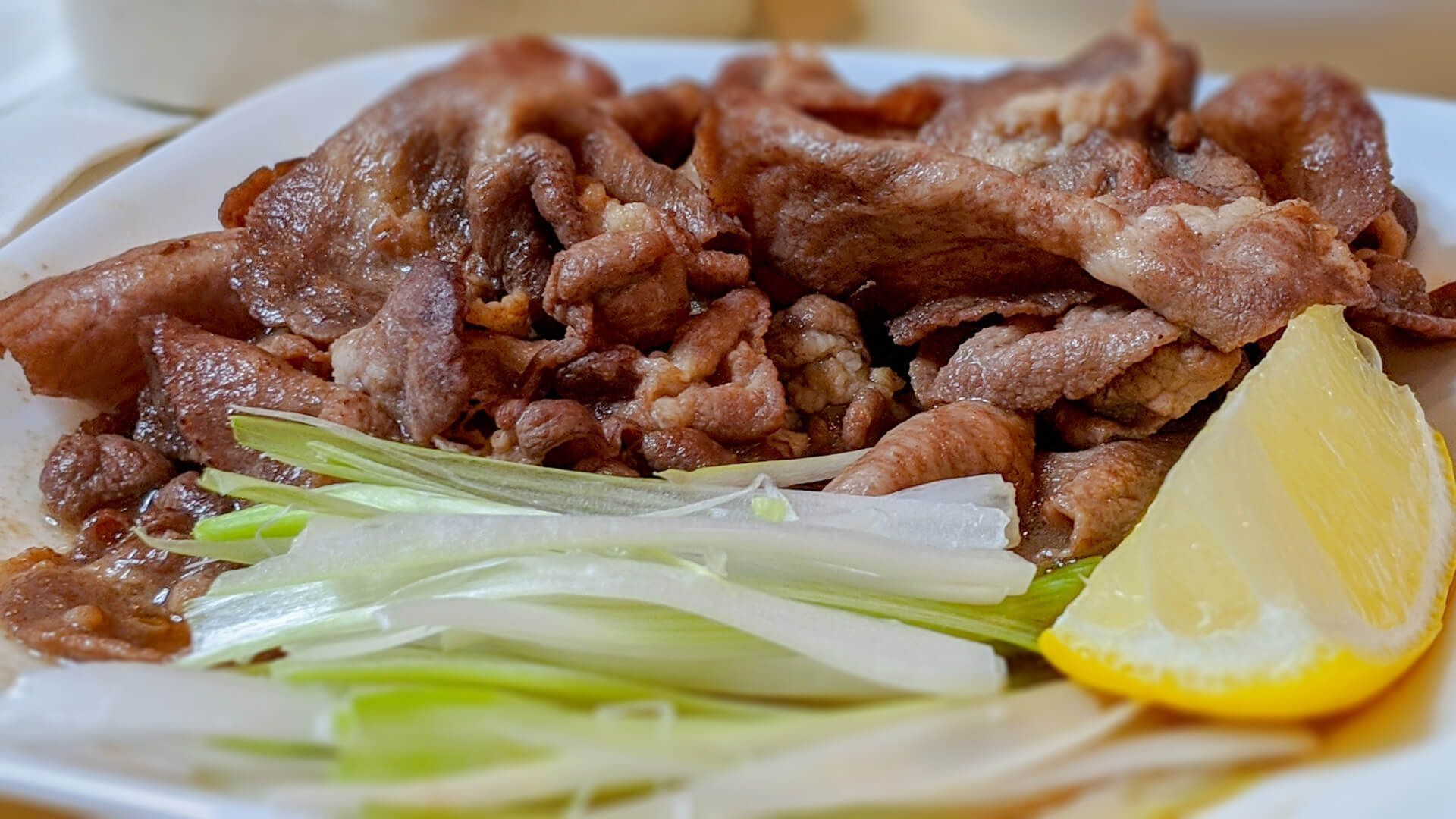 a white plate topped with meat, green onions and a slice of lemon
