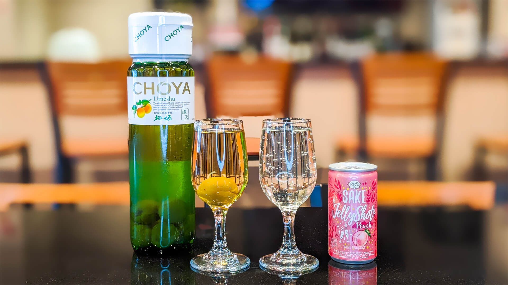 a bottle of choya tea and two wine glasses are on a table