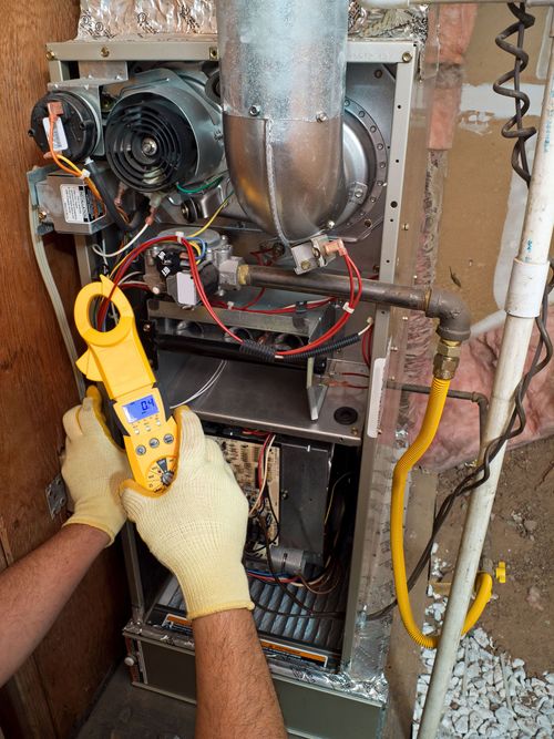 Technician uses a yellow multimeter to test wiring inside an open furnace cabinet.