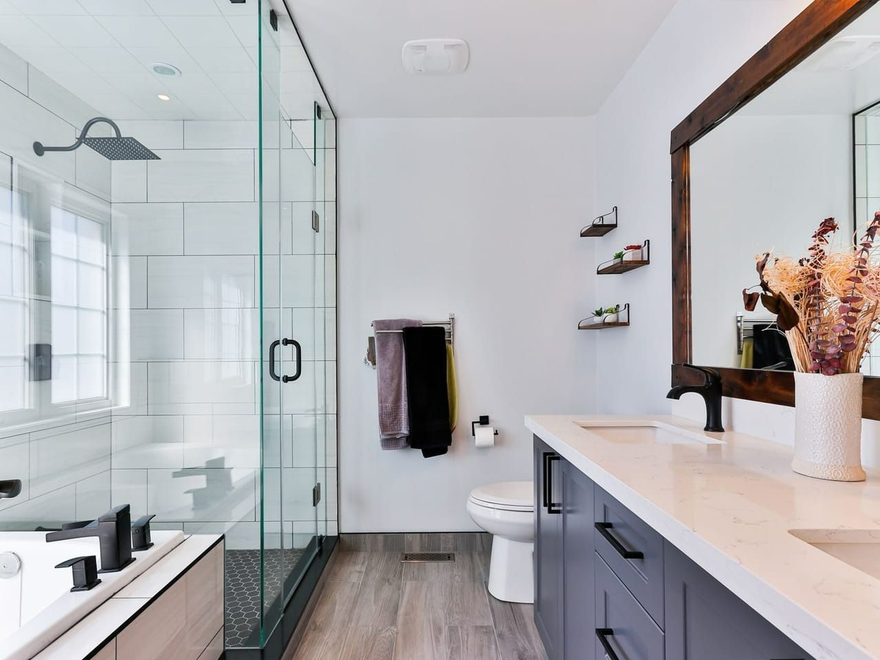 Modern bathroom with glass shower, white tub, dark vanity, and wooden-framed mirror