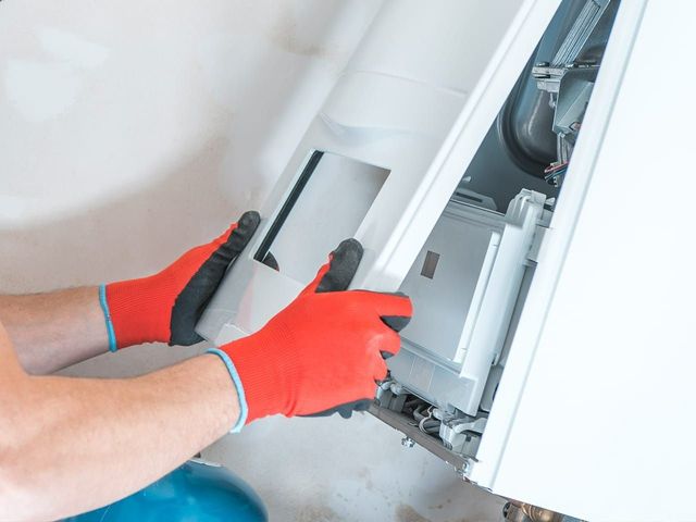 Gloved hands removing a white appliance panel during repair