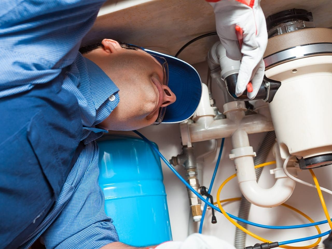 Plumber working under a sink, inspecting pipes with a flashlight and tools