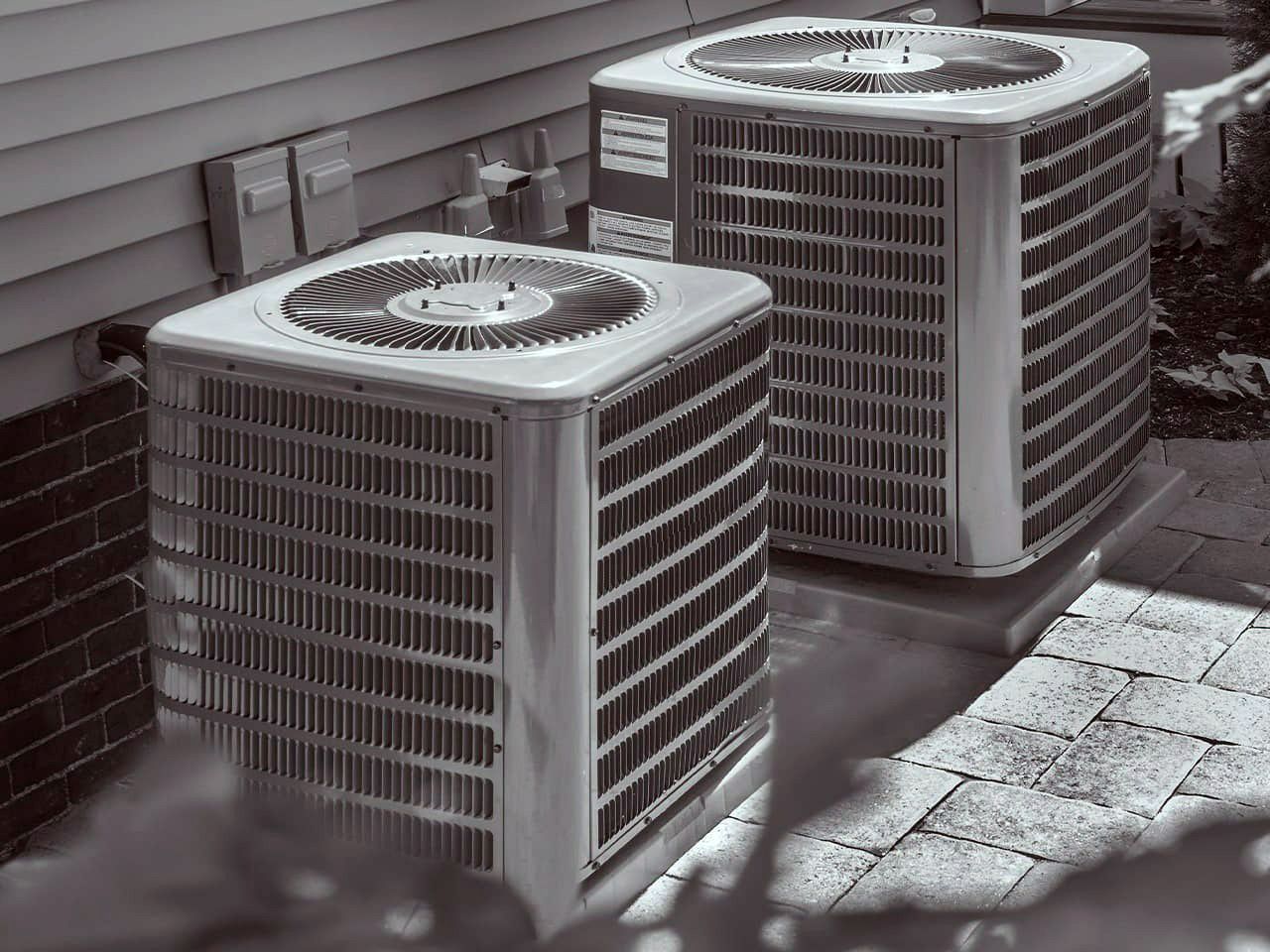 Two outdoor air conditioning units beside a building wall on a paved surface