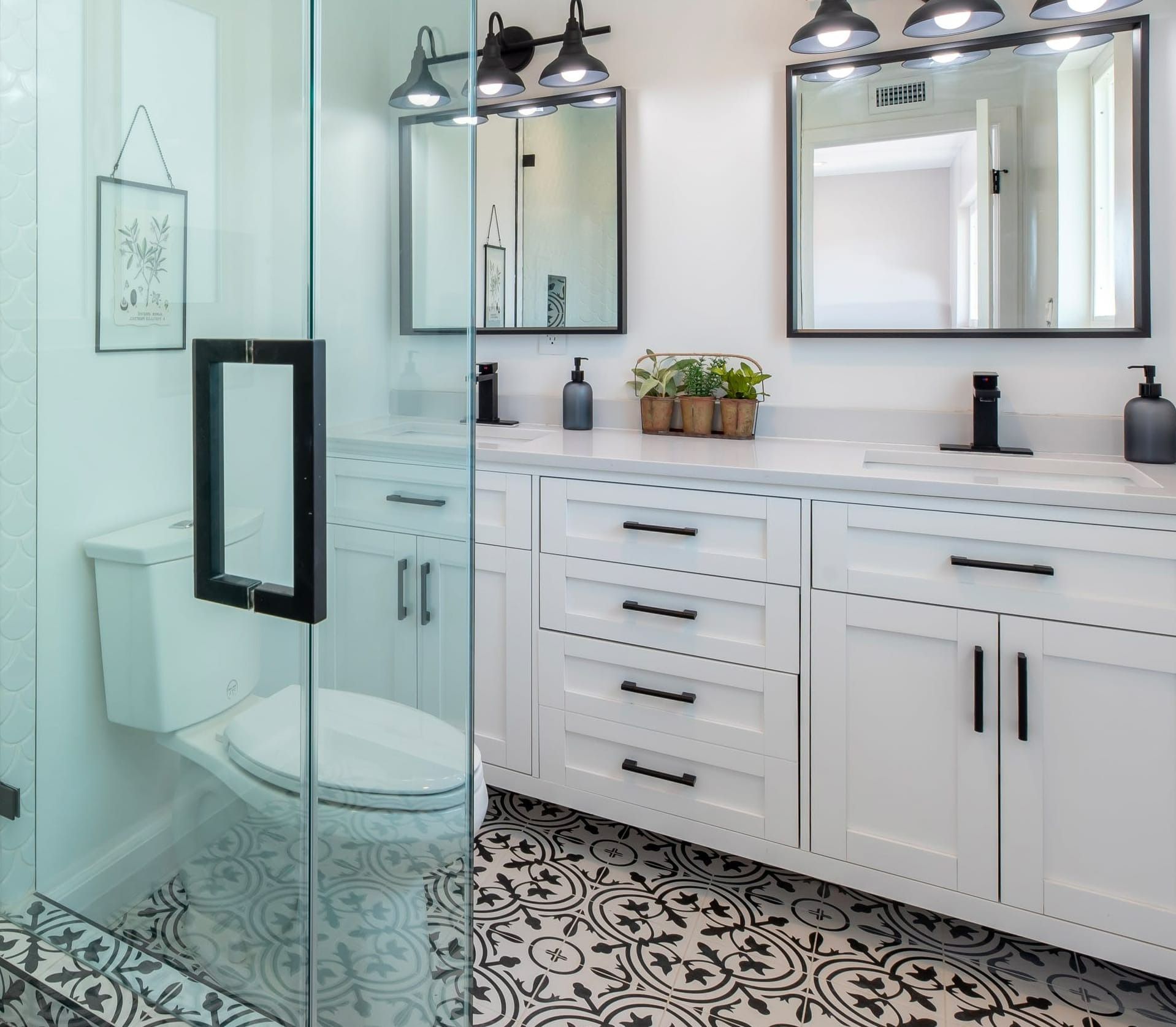 Bright modern bathroom with glass shower, white vanity, mirrors, and patterned black-and-white floor tiles.