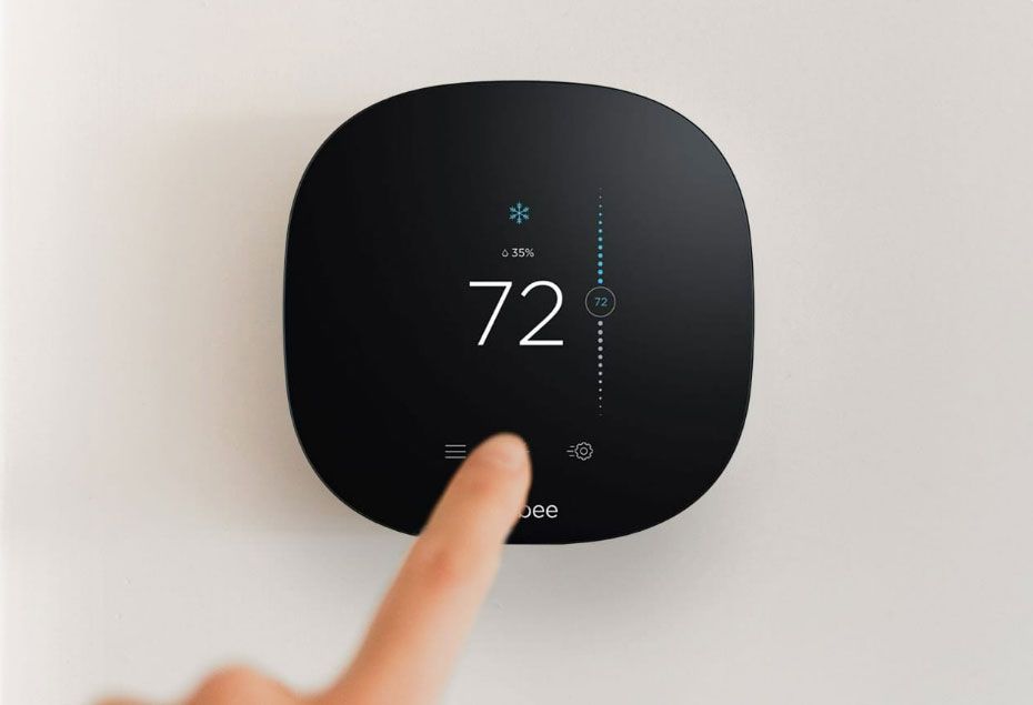 Finger touching a black digital thermostat displaying 72° on a white wall