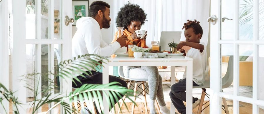 Family sharing a meal at a bright dining table with plants in the foreground