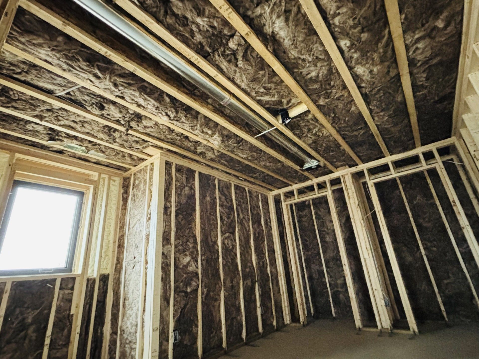 Interior view of a room under construction with exposed wooden framing and insulation.