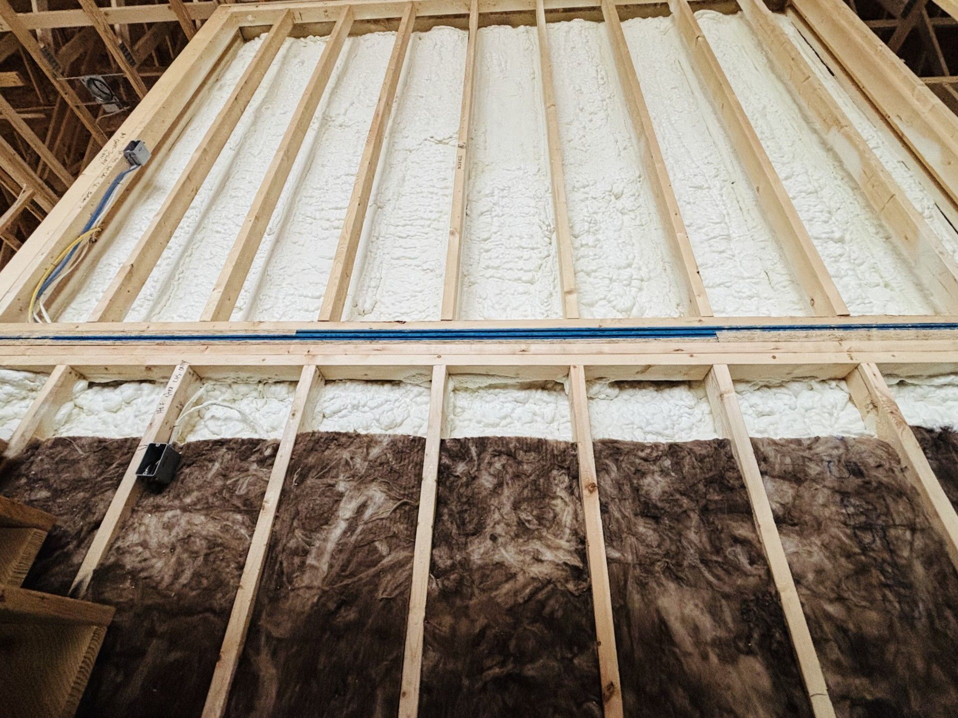Wooden wall frame with spray foam insulation above and brown insulation below.