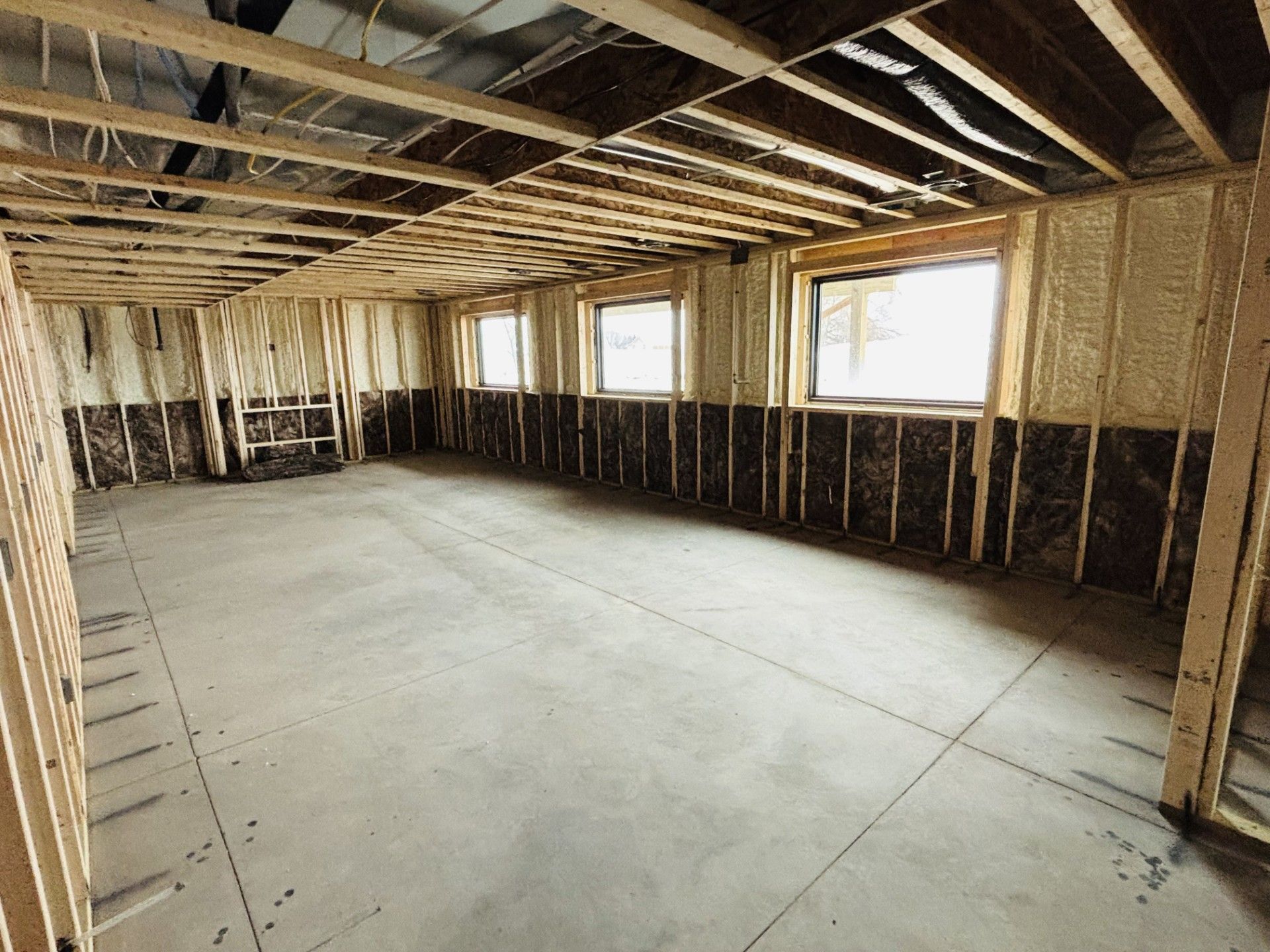 Unfinished basement with wooden framing, spray foam insulation, three windows, and concrete floor.