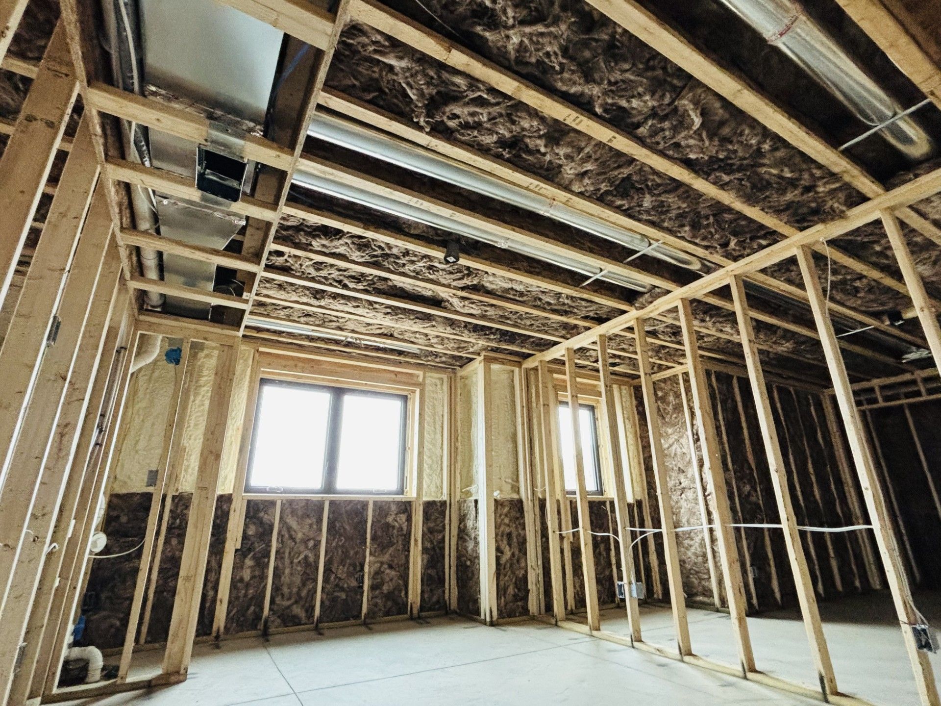 Interior view of a room under construction with exposed wooden framing and insulation in the walls and ceiling.