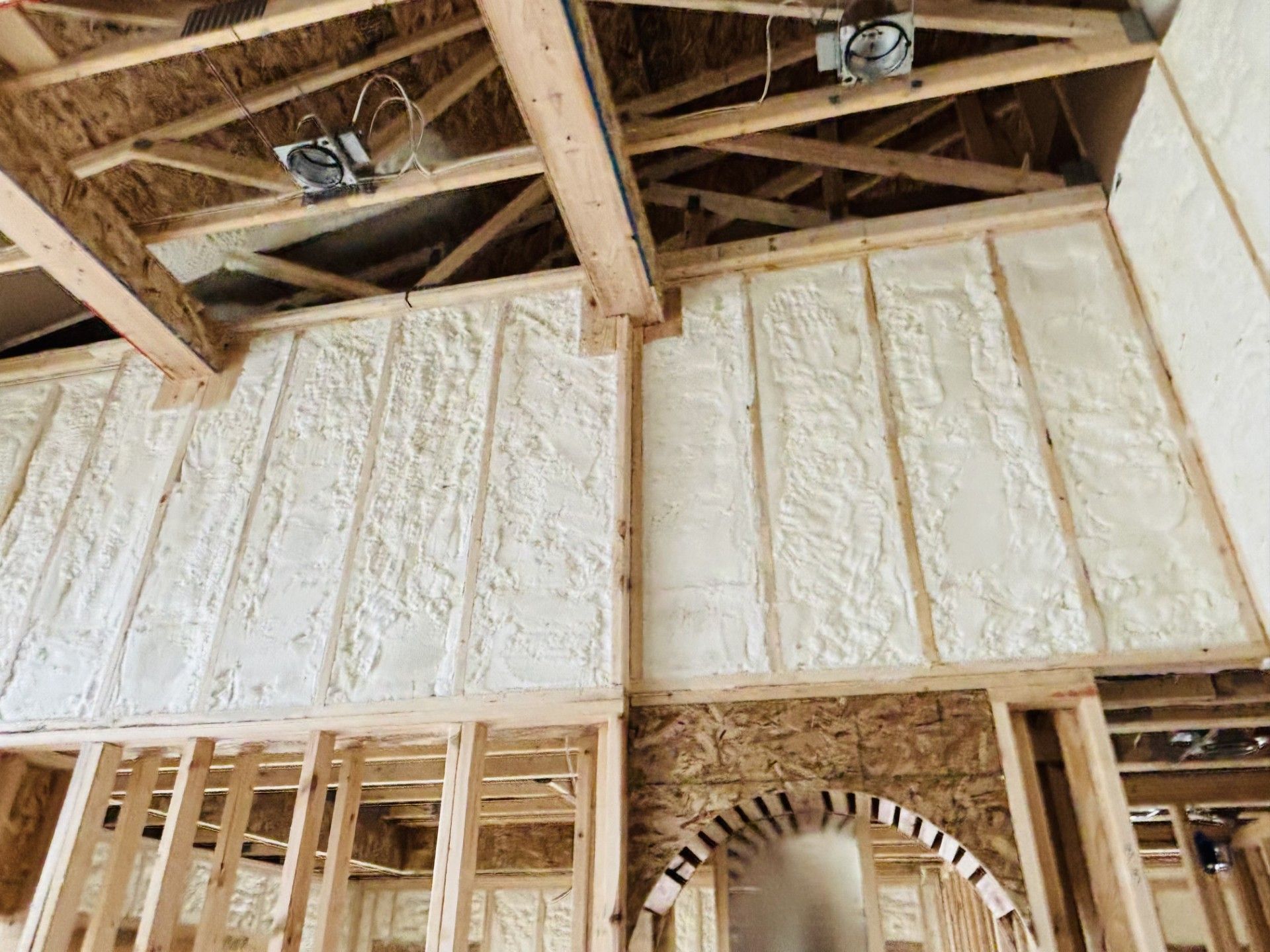 Interior of a house under construction; walls are sprayed with white foam insulation, exposed wooden beams and framing.