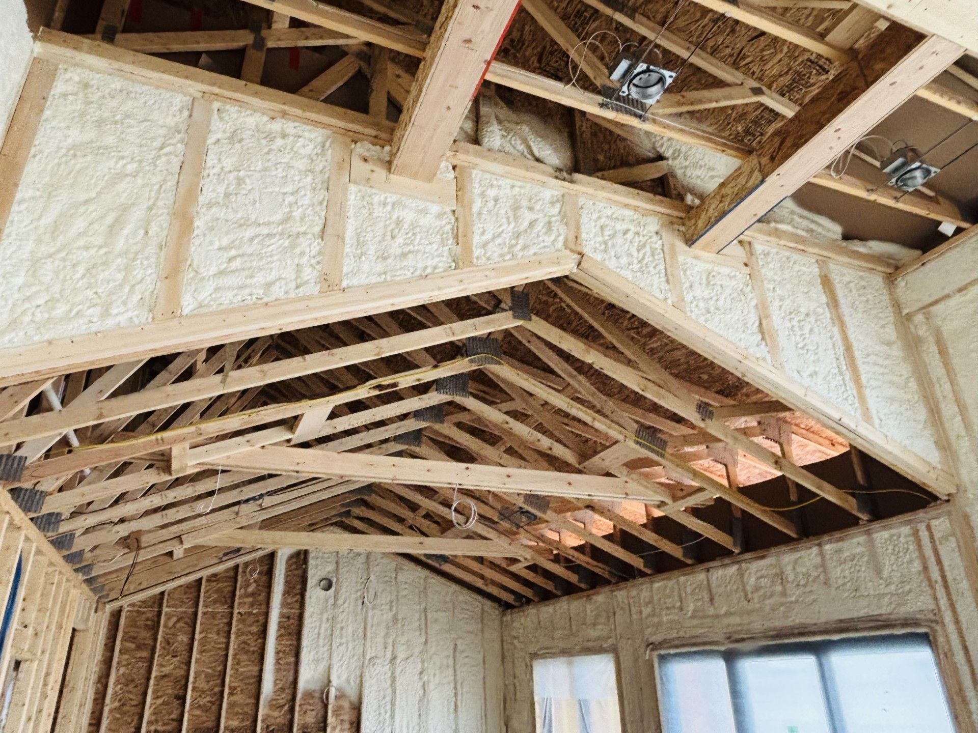 Interior of a building under construction, spray foam insulation on walls and ceiling framework, natural wood, unfinished.