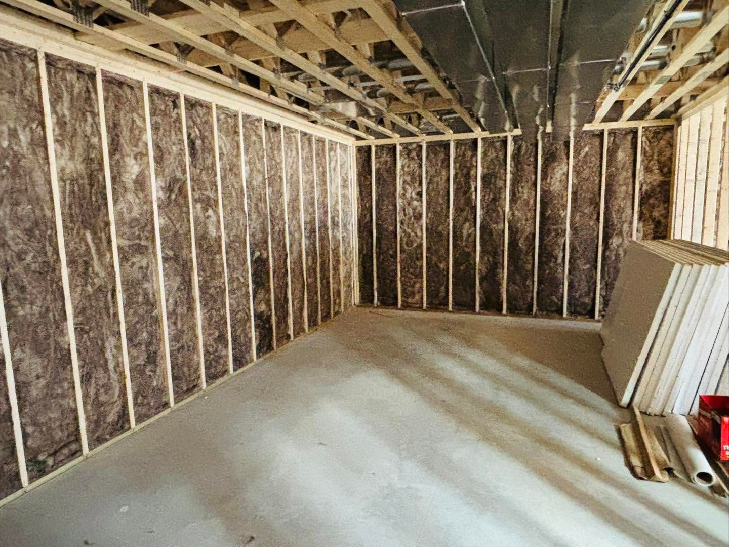 Unfinished room with exposed wall insulation, open ceiling joists, and a concrete floor