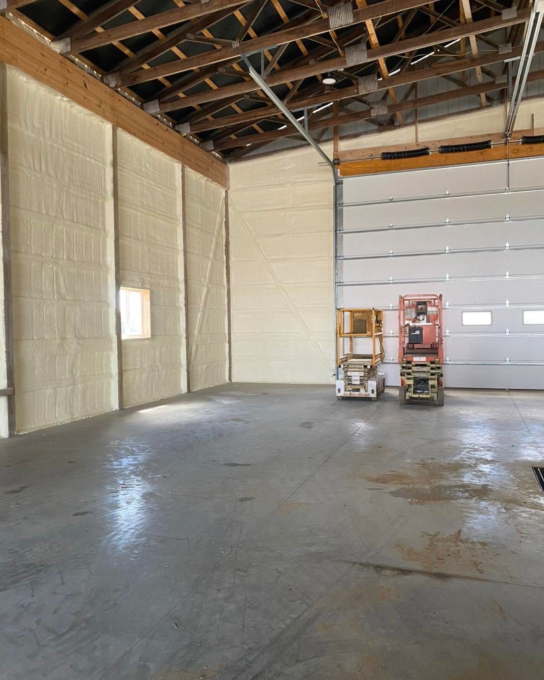 Empty warehouse interior with exposed rafters, concrete floor, and a large white overhead door.