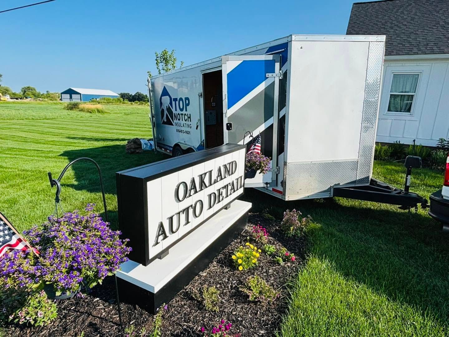 Oakland Auto Detail sign beside a white trailer on a grassy lawn