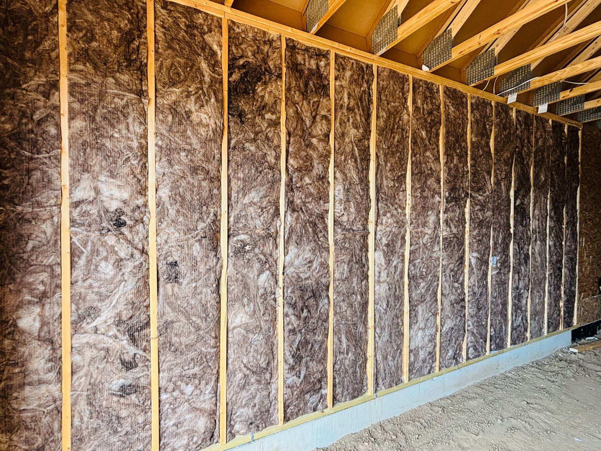 Insulation installed between wooden studs in a construction project; rafters visible.