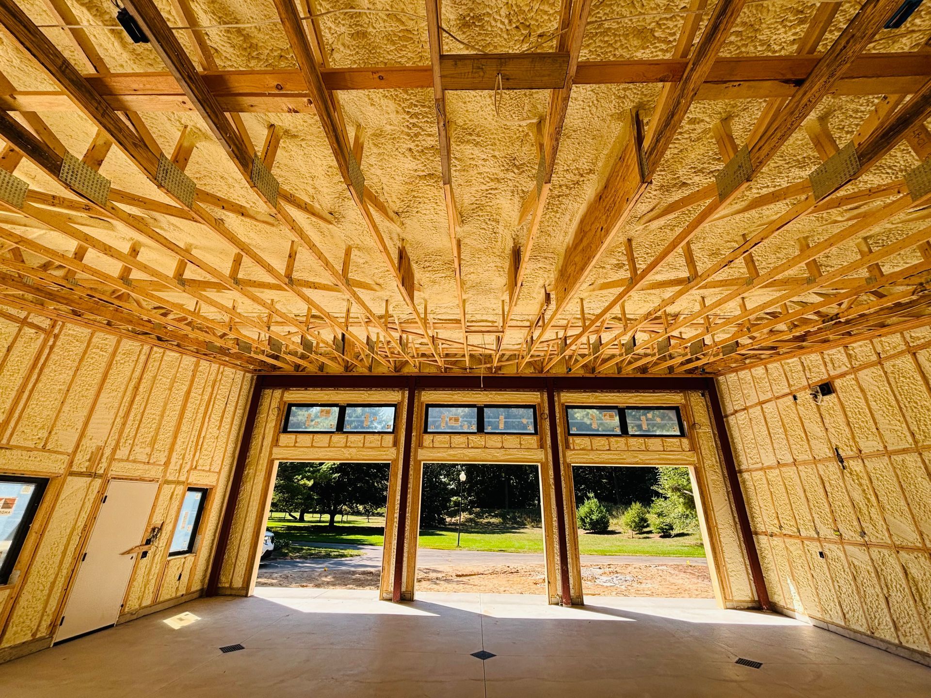 Interior view of a building under construction, insulated with yellow spray foam, framed by wood, with open doorways.