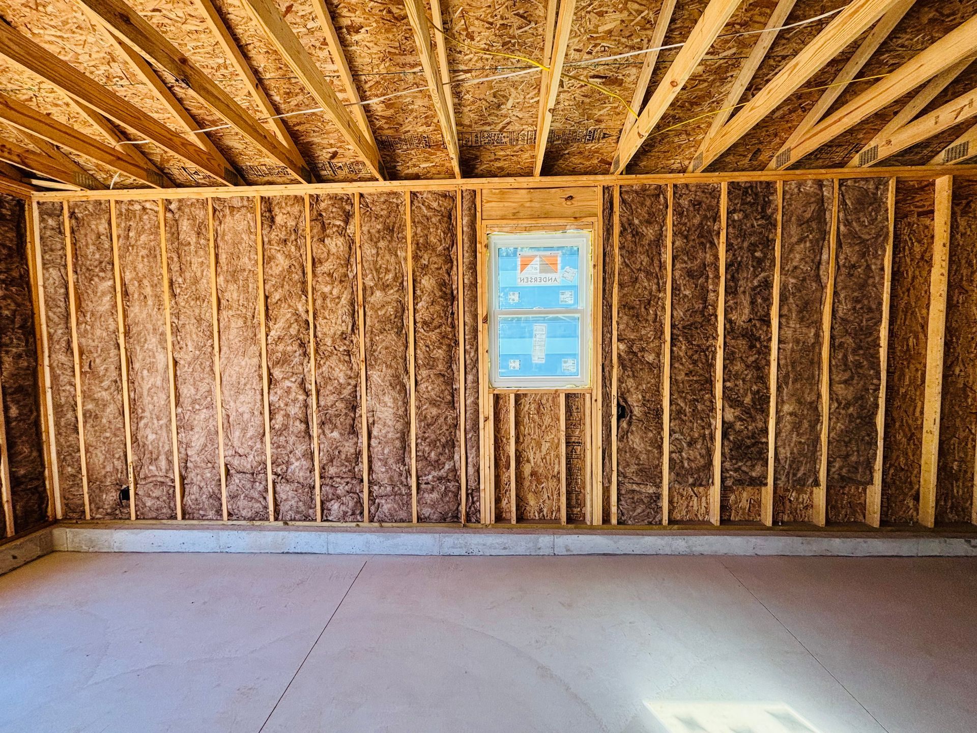 Interior view of a building under construction, featuring wooden framing, insulation, a window, and a concrete floor.