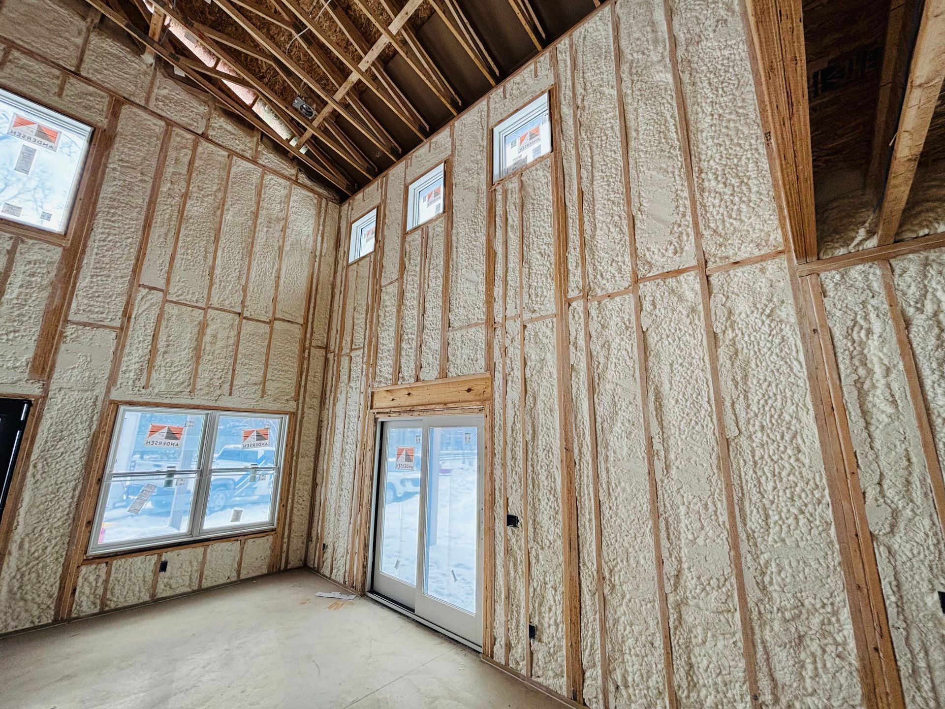 Interior of a building under construction, walls covered with spray foam insulation, wood framing visible.