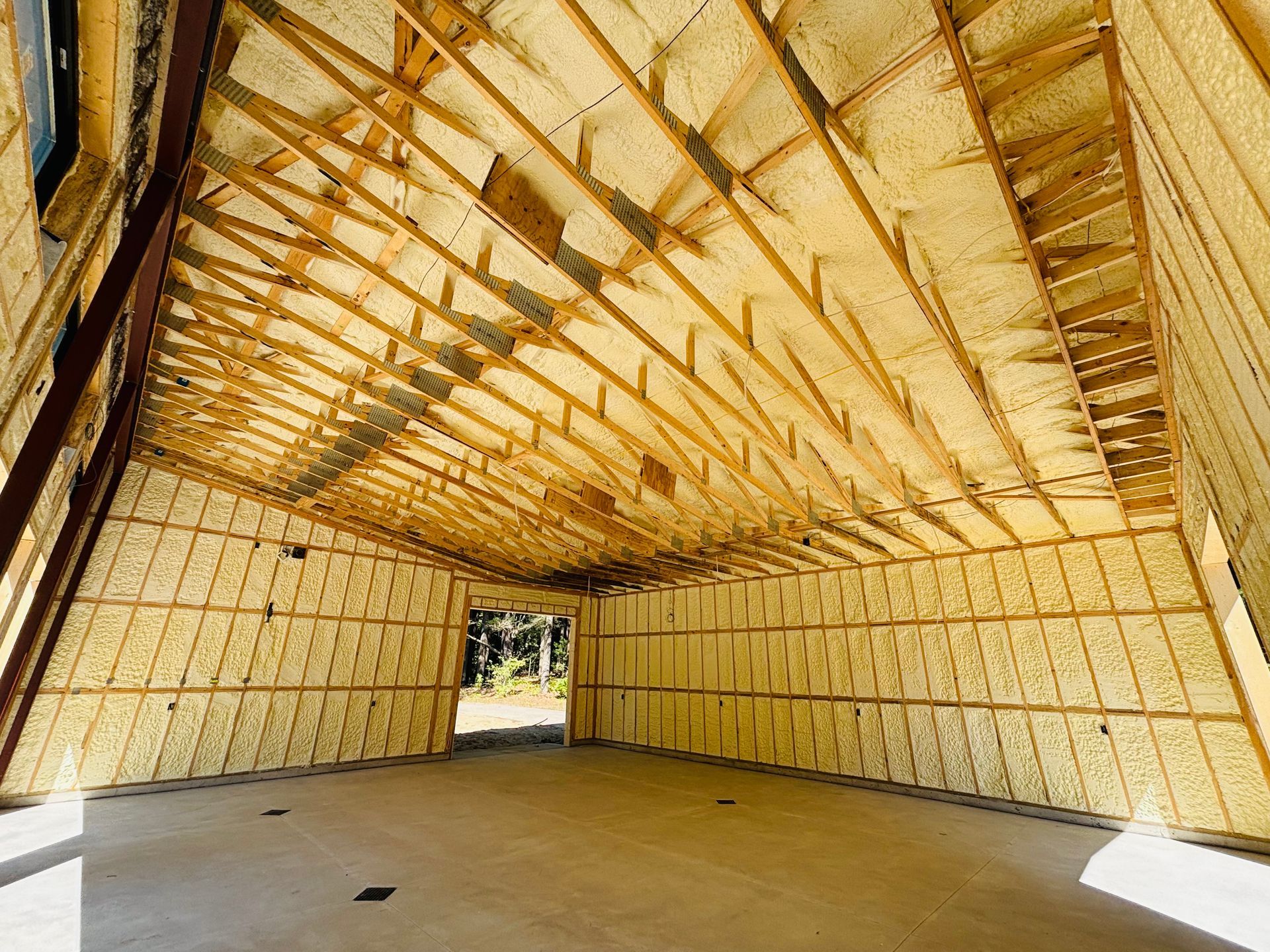 Interior of a building under construction, insulated with yellow foam, with wooden beams and a concrete floor.
