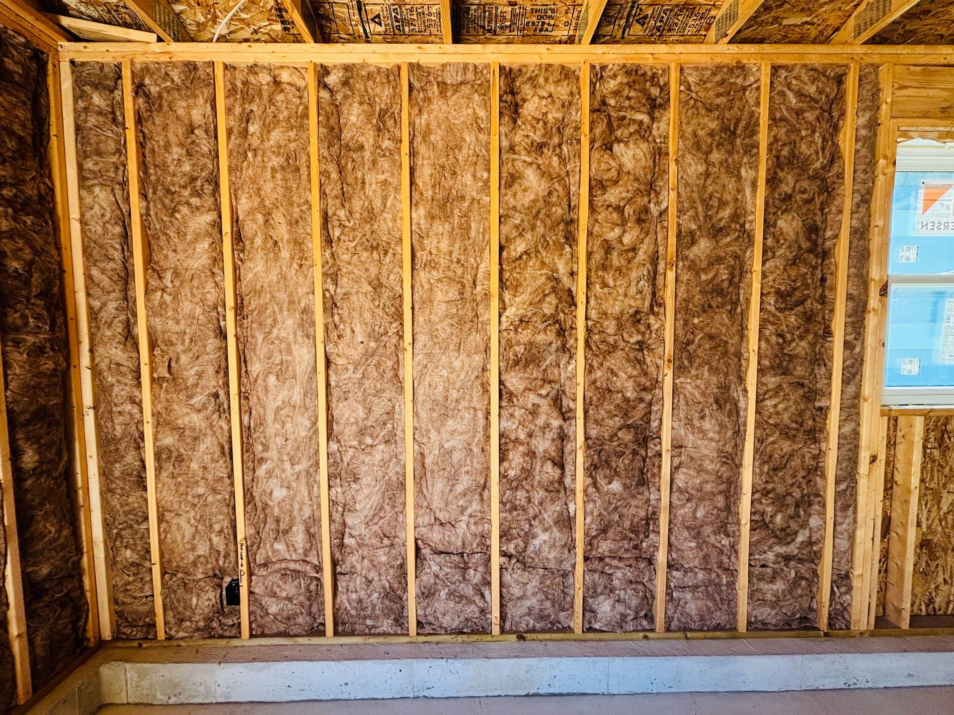 Insulated interior wall of a building under construction; wooden studs with brown insulation.