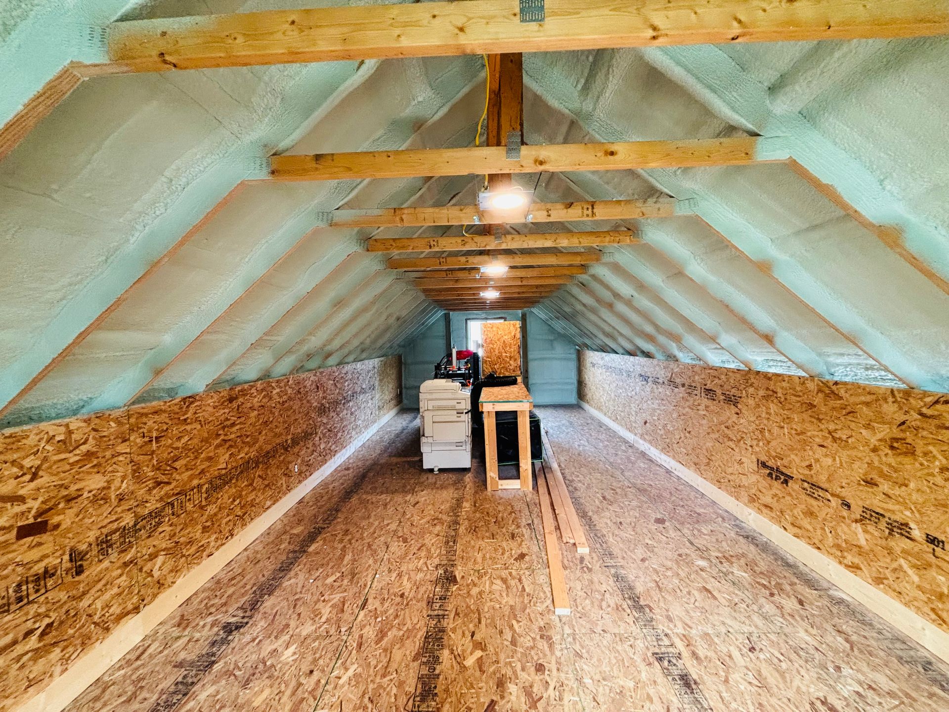 Attic interior with spray foam insulation, exposed wooden beams, and oriented strand board walls and floor.