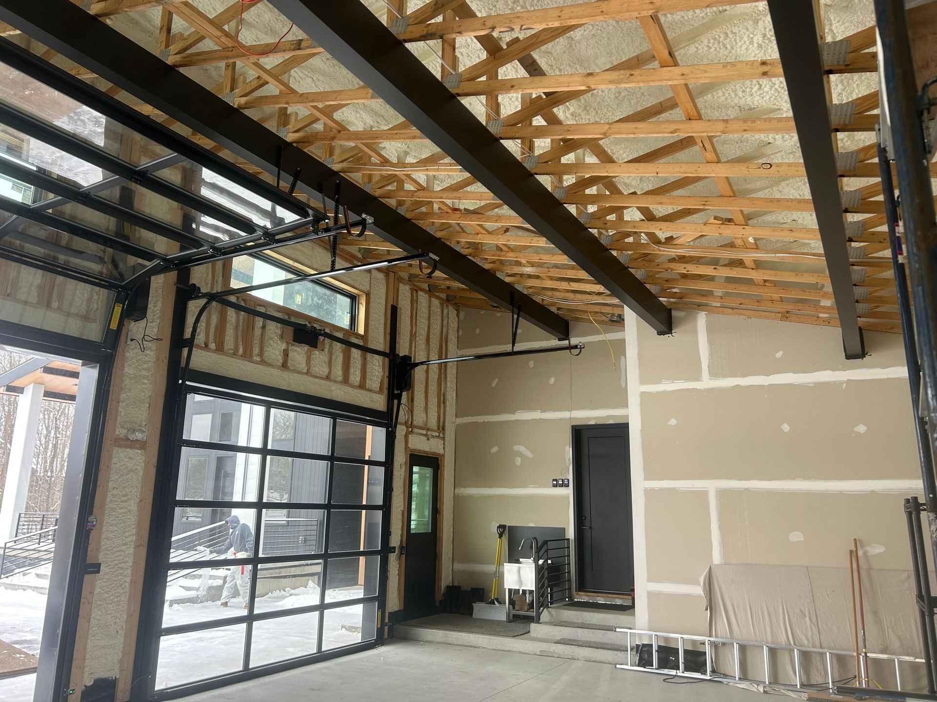 Garage under construction with glass door, exposed beams, and unfinished walls.