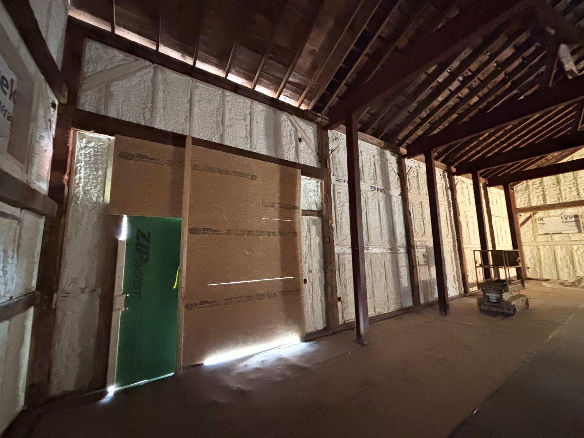 Interior of a barn undergoing renovation. Walls are insulated with spray foam. A green door is visible.