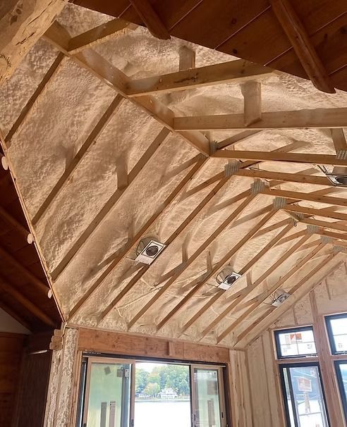 Interior view of a vaulted ceiling with spray foam insulation applied to the rafters. Windows and lights are visible.