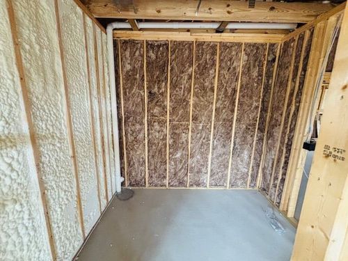 Room under construction: studs, insulation, spray foam, concrete floor, pipes.