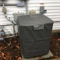 An air conditioner is sitting outside of a house with a cover on it