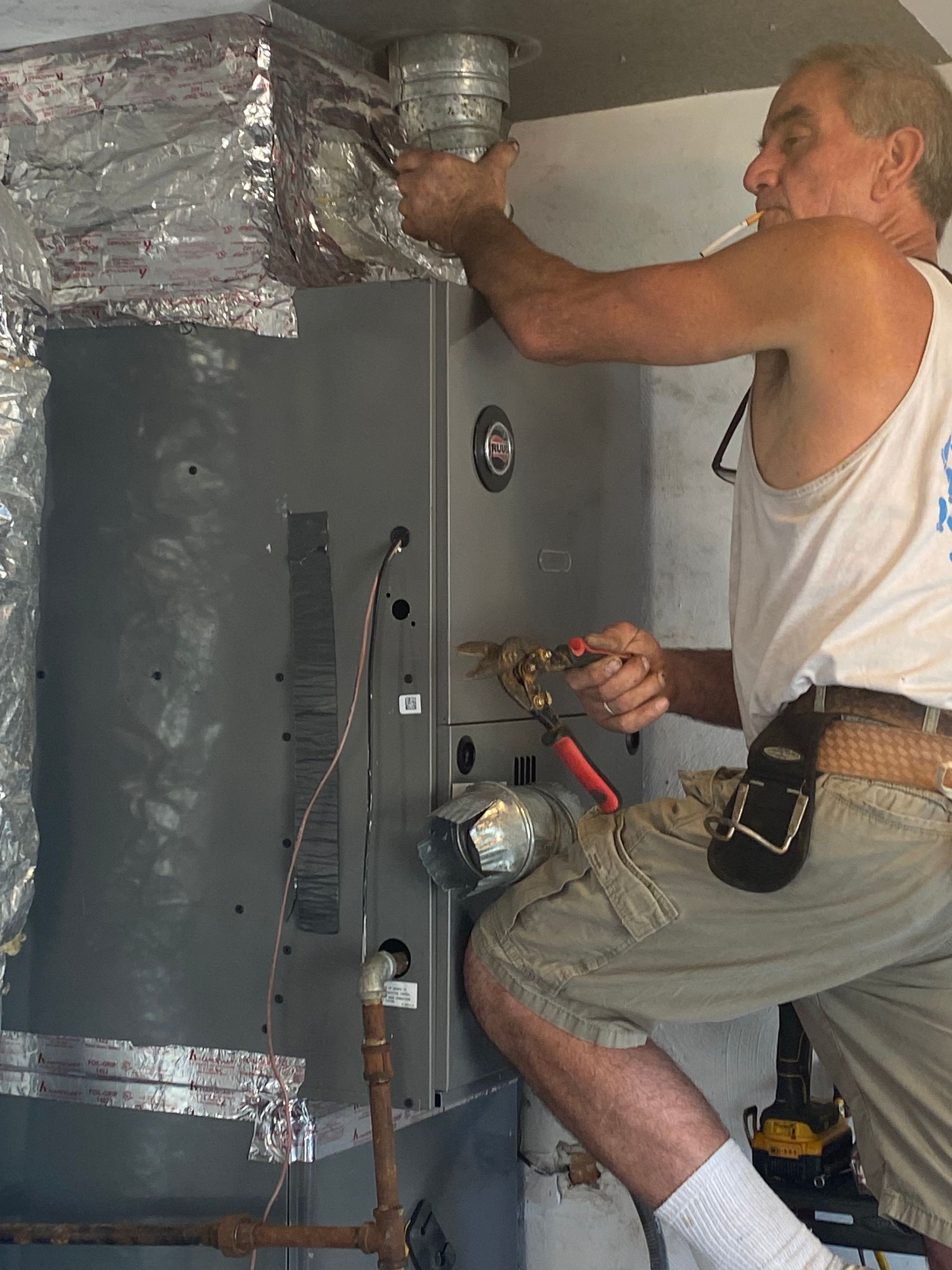 A man in a white tank top is working on an air conditioner