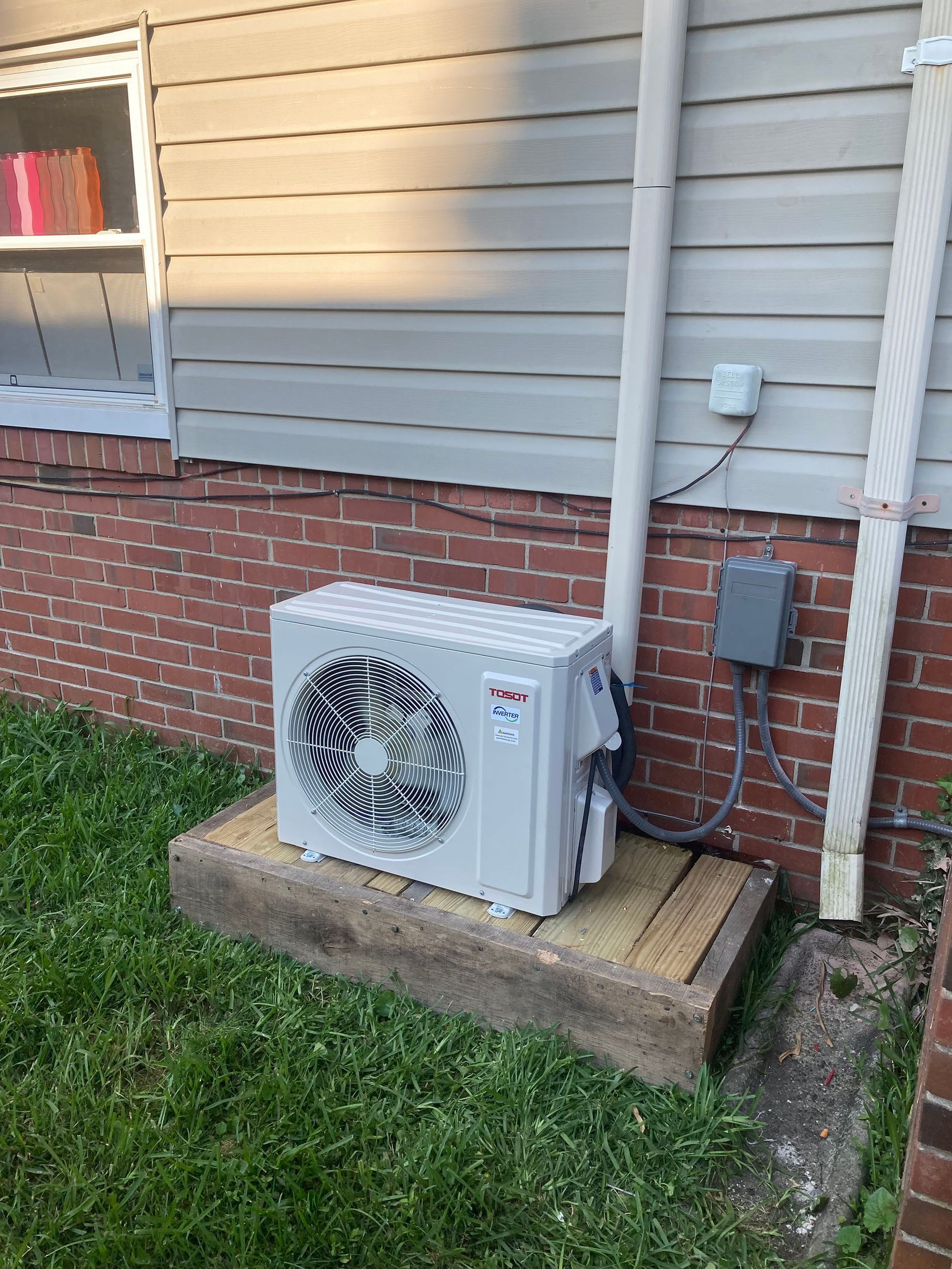 A white air conditioner is installed on the side of a brick house