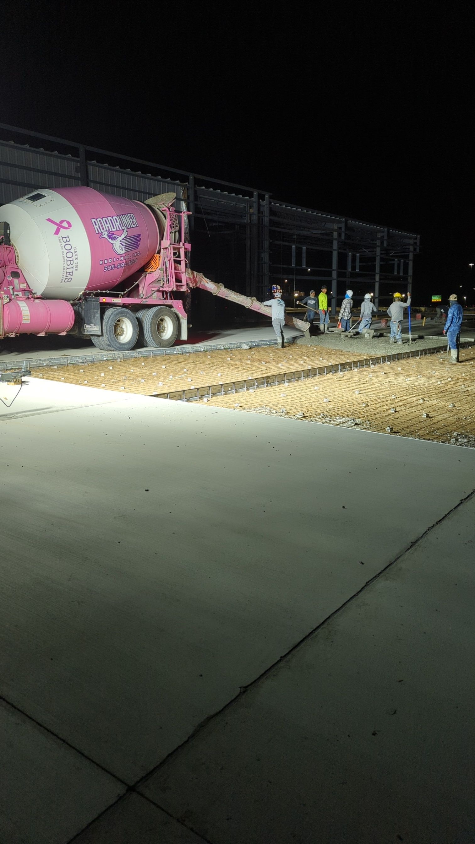 A concrete mixer truck is pouring concrete into a concrete driveway at night.