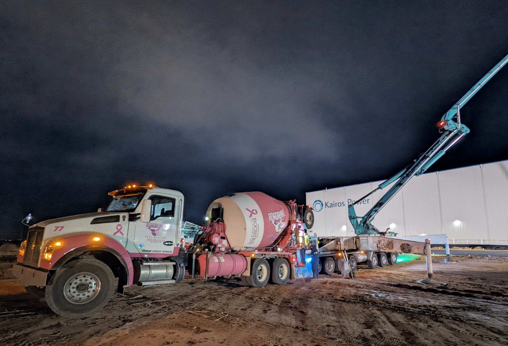 A concrete mixer truck is driving down a dirt road at night.