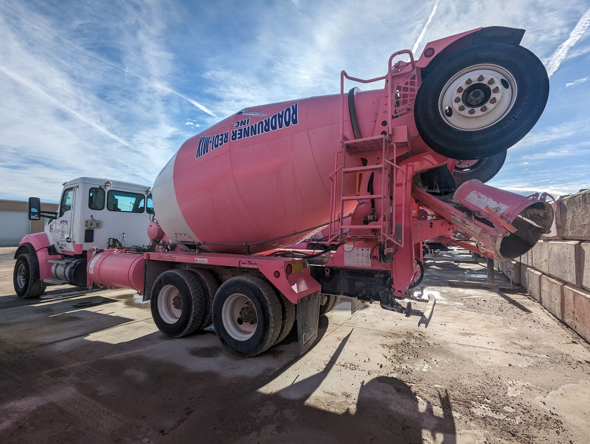 A pink and white concrete mixer truck is parked on the side of the road.