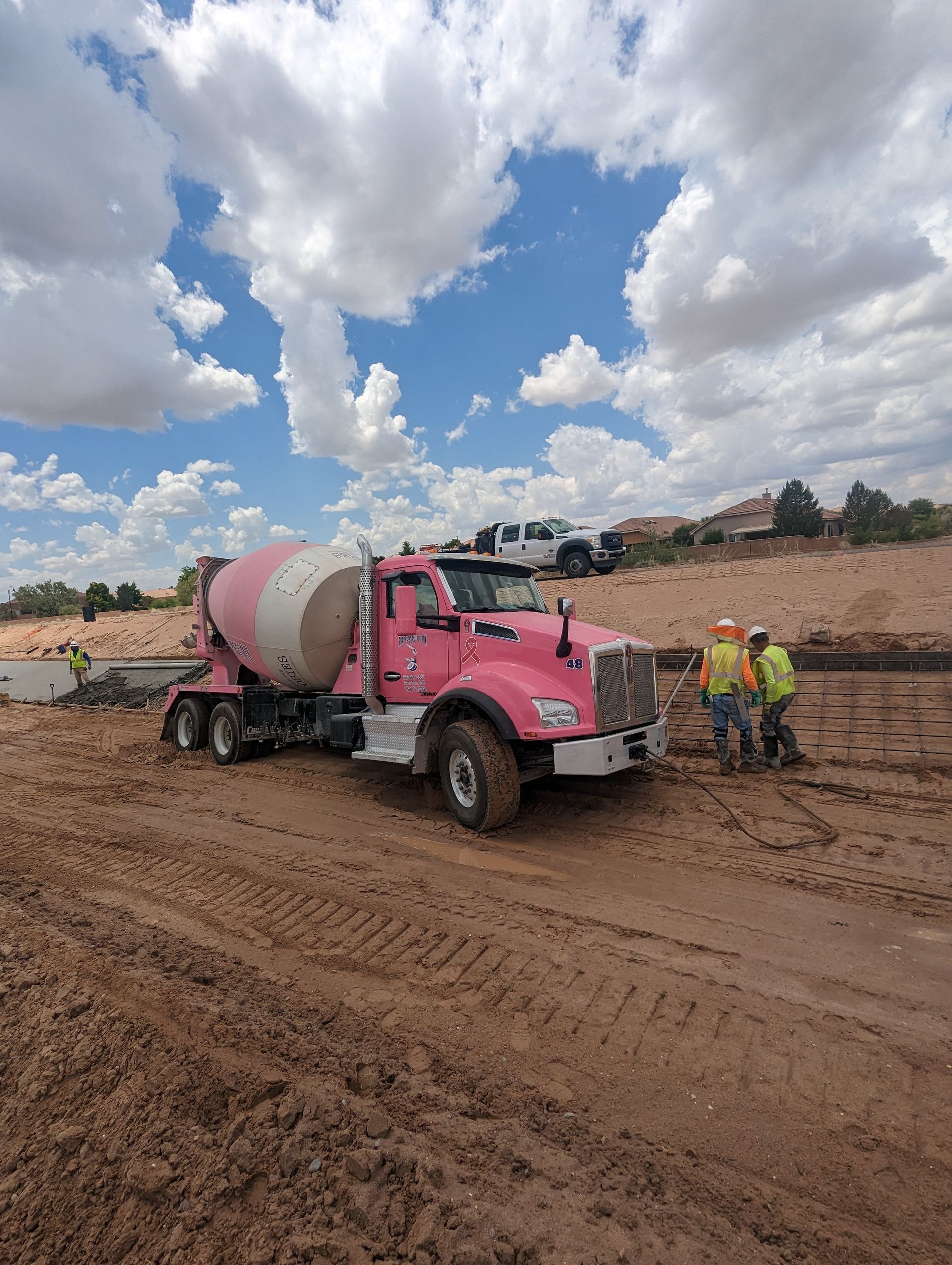 A pink concrete mixer truck is driving down a dirt road.