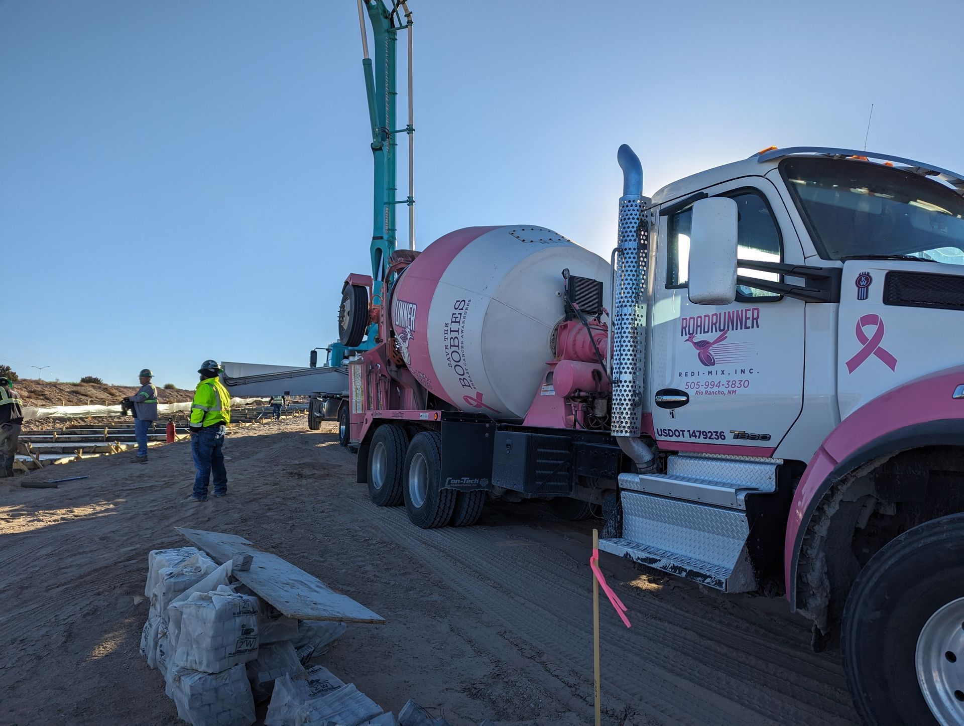 A pink and white truck with a breast cancer ribbon on the side is parked on a dirt road.