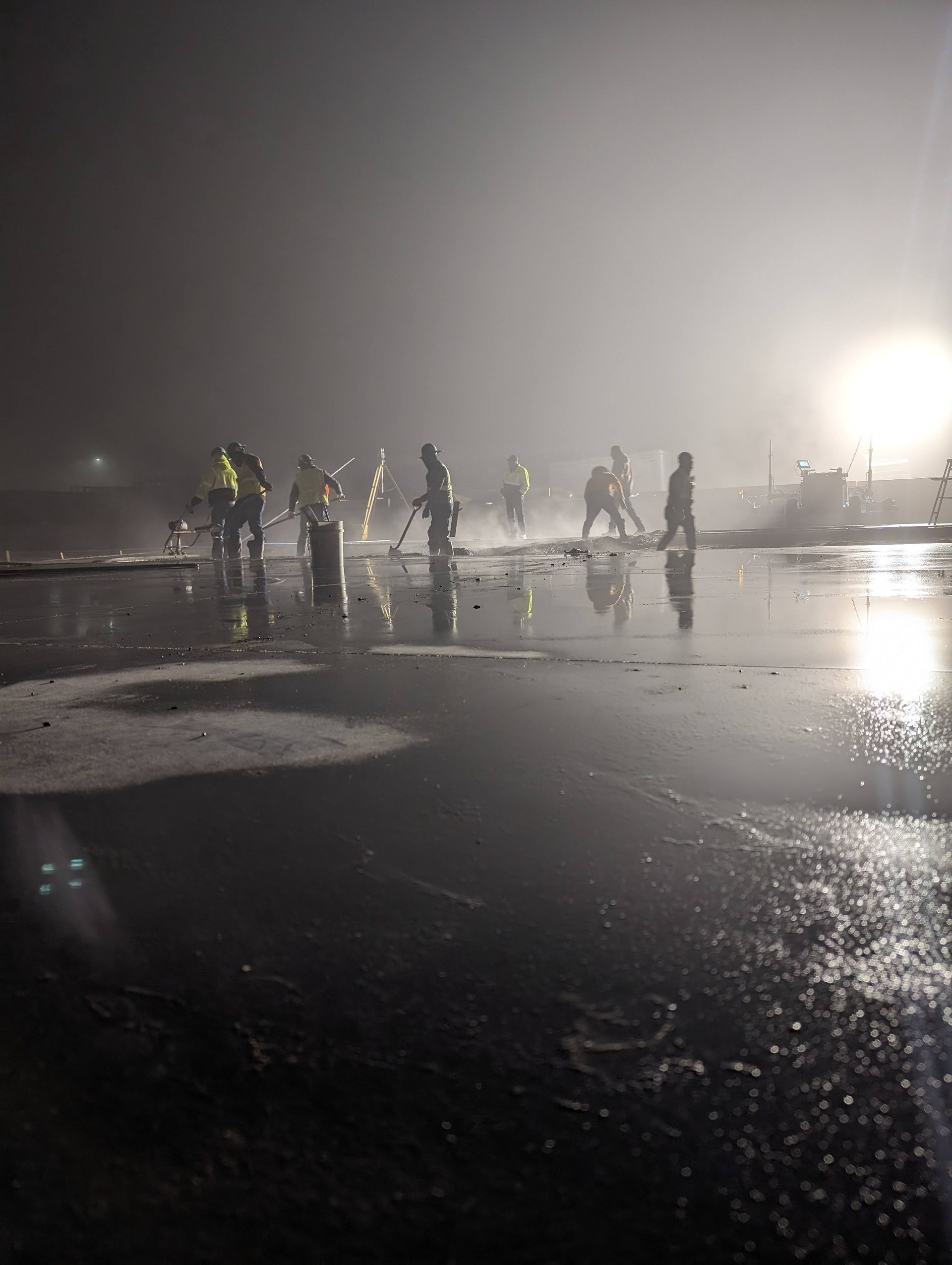 A group of people are walking on a wet road at night.