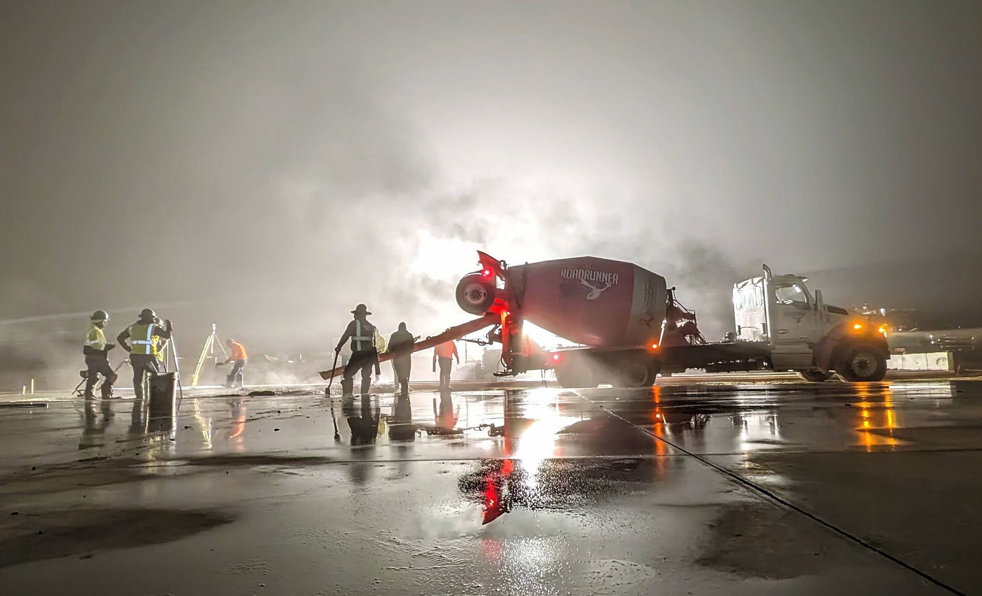A concrete mixer is pouring concrete on a wet runway at night.