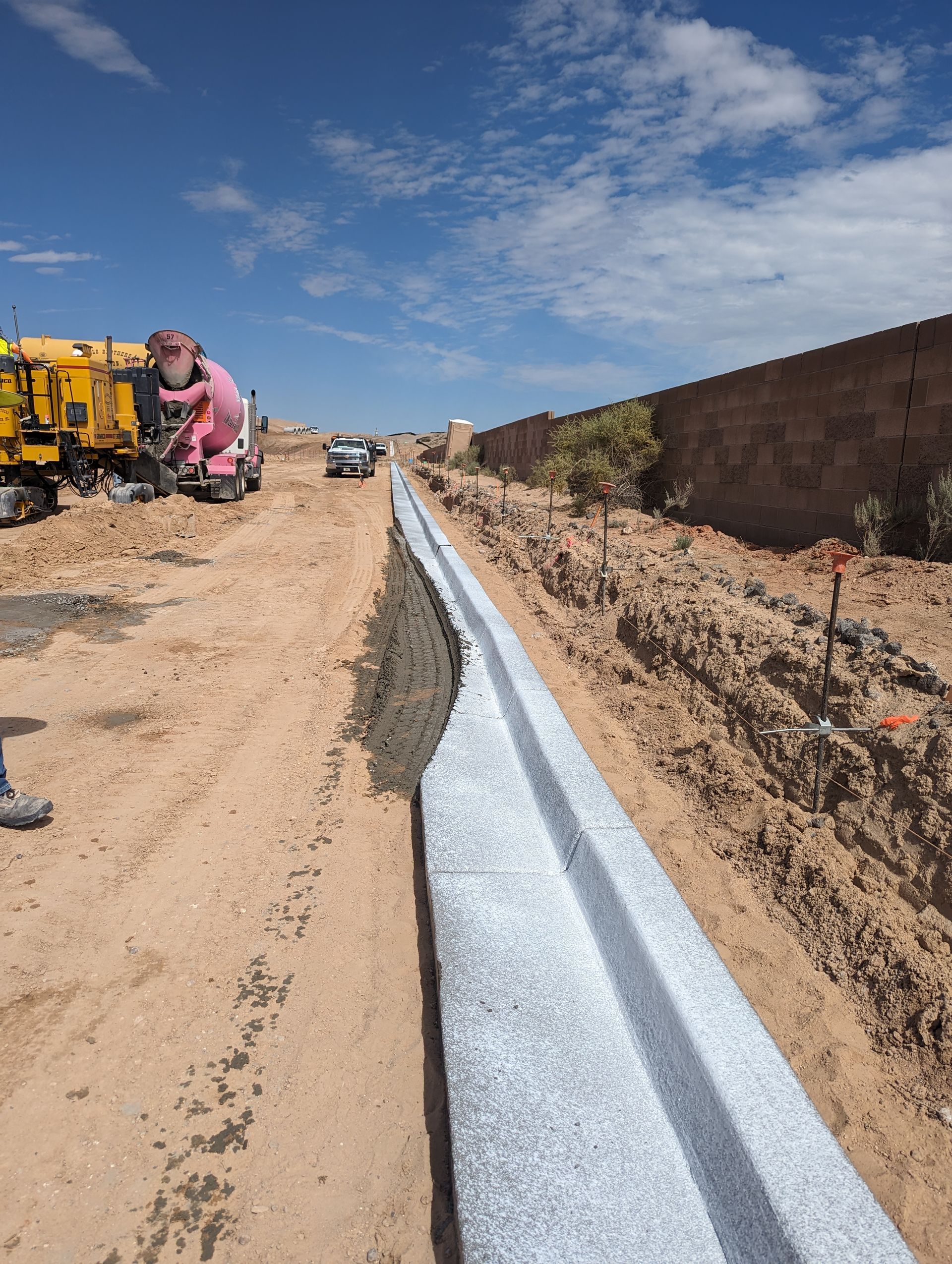 A concrete mixer is pouring concrete into a trench on a dirt road.