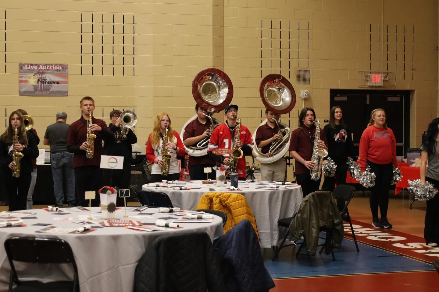 A band in red and white uniforms plays at an event with round tables.
