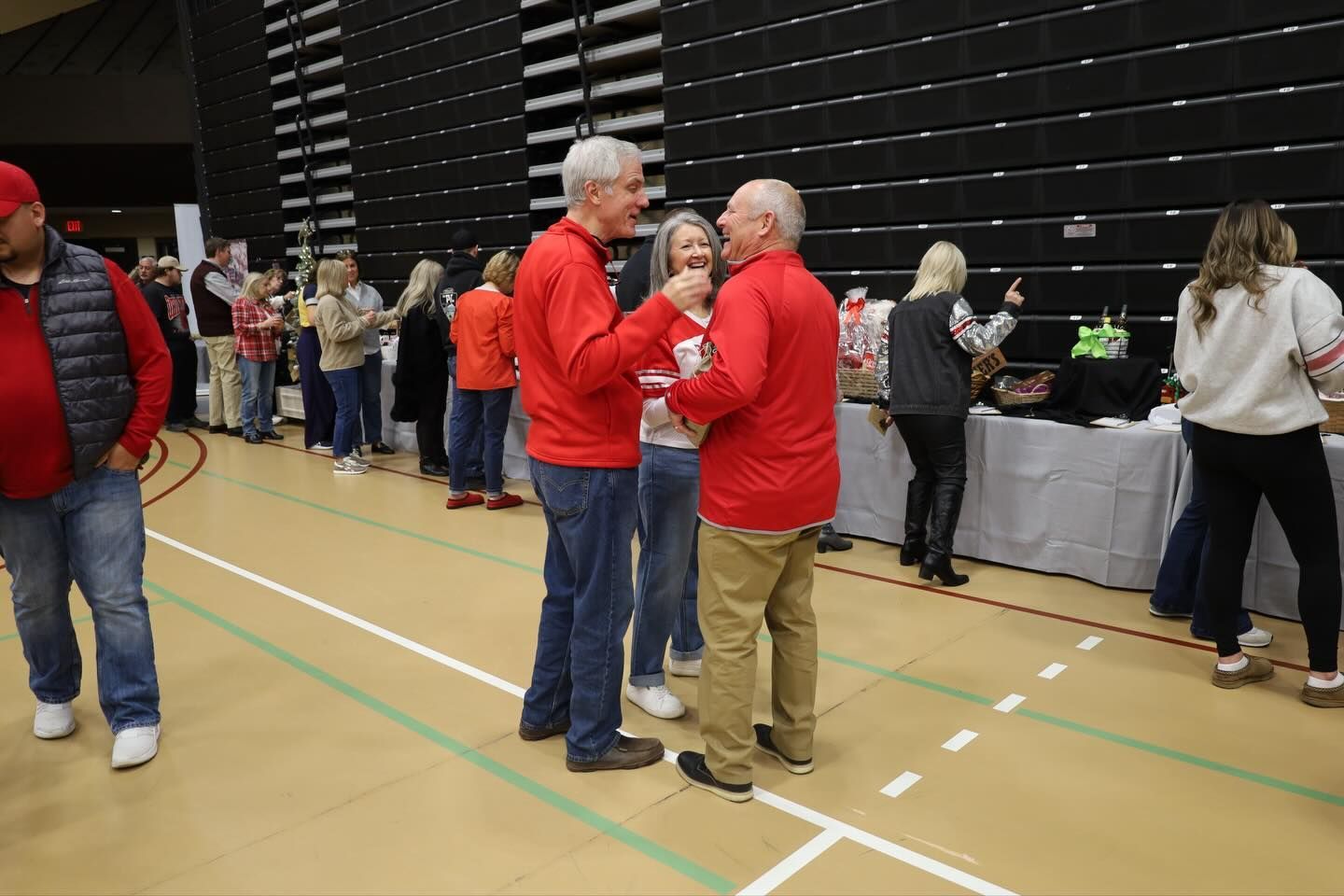 People in red shirts talking in an indoor space with others in line.