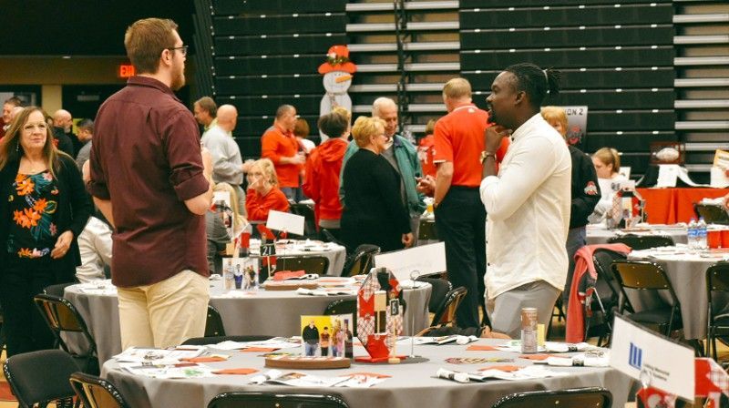 A group of people are standing around tables in a gym.
