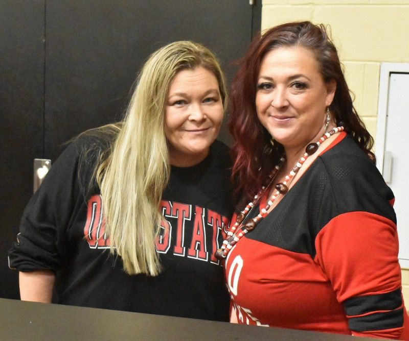 Two women are posing for a picture and one is wearing a shirt that says all state
